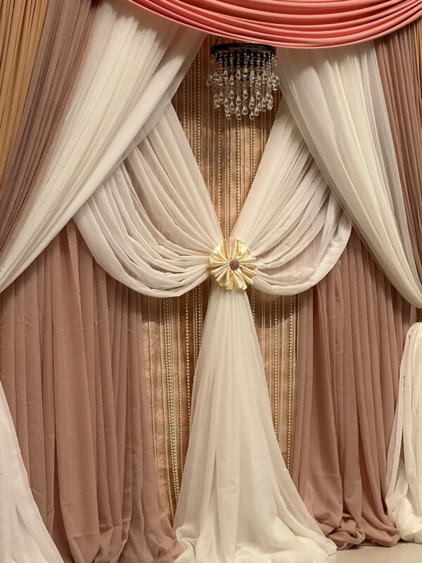 Elegant wedding backdrop with blush, ivory, and champagne draping, accented with crystal beads and a chandelier by SWFL Wedding & Event Rentals