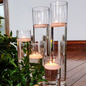 Floating candles in clear cylinder vases surrounded by greenery – romantic wedding décor by SWFL Wedding & Event Rentals