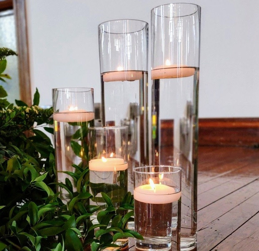 Floating candles in clear cylinder vases surrounded by greenery – romantic wedding décor by SWFL Wedding & Event Rentals