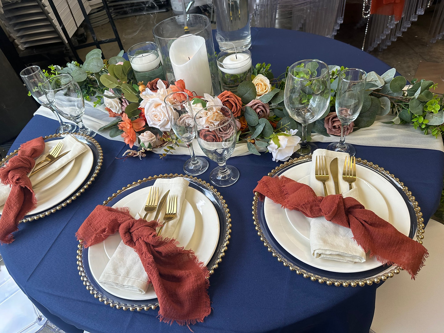 Elegant wedding table with navy linen, gold flatware, pearl charger plates, and a floral garland centerpiece by SWFL Wedding & Event Rentals