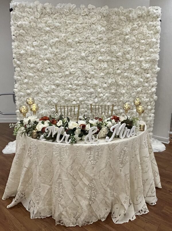 Elegant wedding table setup with white linens and a white floral backdrop by SWFL Wedding & Event Rentals