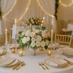 Elegant Naples wedding reception table featuring gold Chiavari chairs, blush and ivory floral centerpiece, gold-accented table settings, tapered candles, and warm string lighting—showcasing elevated rental décor options from SWFL Wedding & Event Rentals.